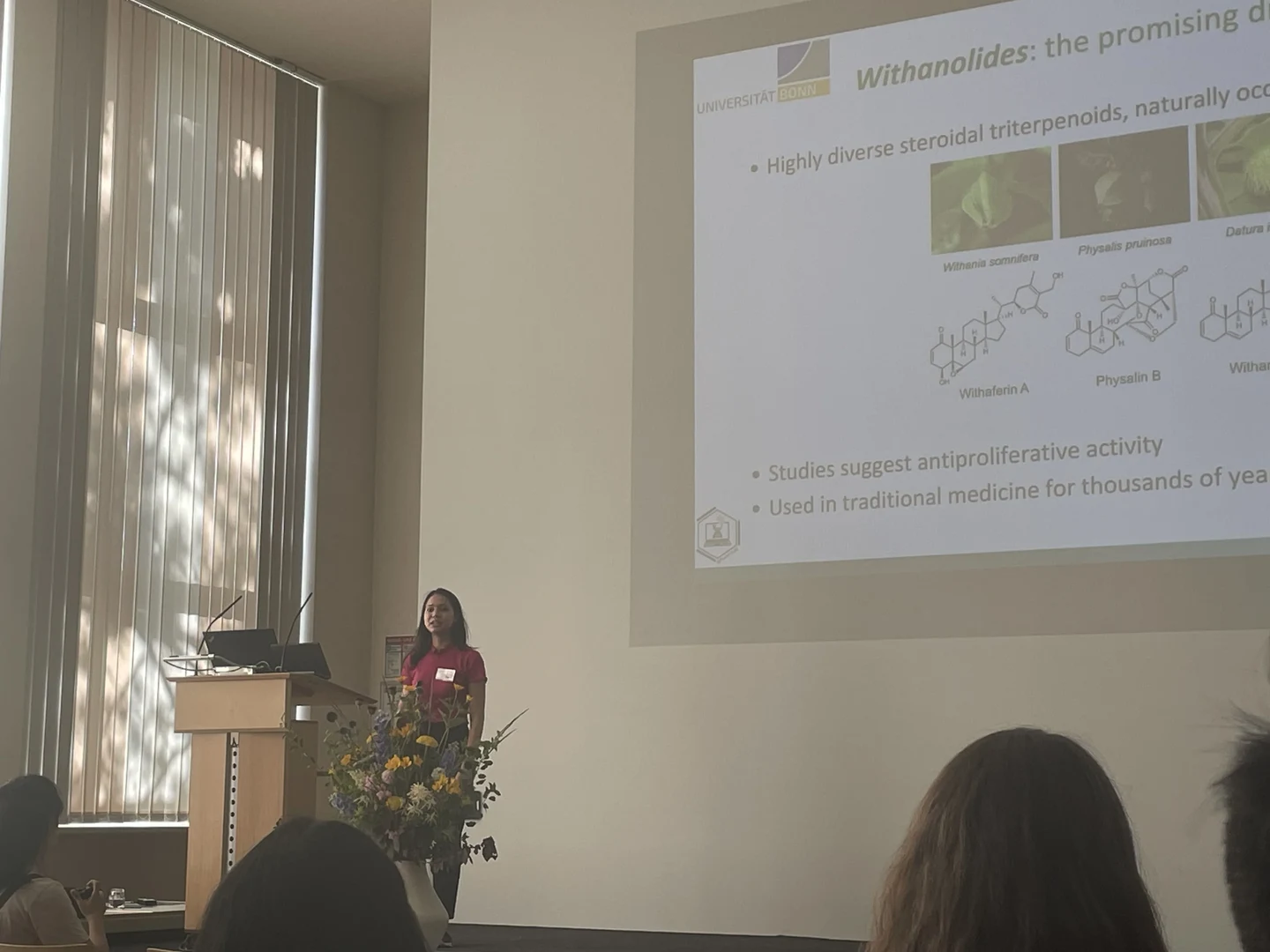 Eine Wissenschaftlerin und ein Wissenschaftler arbeiten hinter einer Glasfassade und mischen Chemikalien mit Großgeräten.